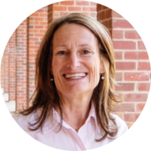 Professional headshot of woman in pink button-down shirt with brick column background