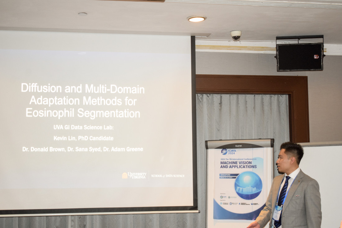 Kevin Lin in suit presenting at conference with screen showing title Diffusion and Multi-Domain Adaptation Methods for Eosinophil Segmentation