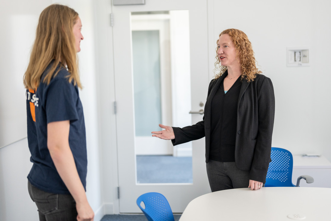 Two women speak in a meeting room, one is a student and the other is an adult 
