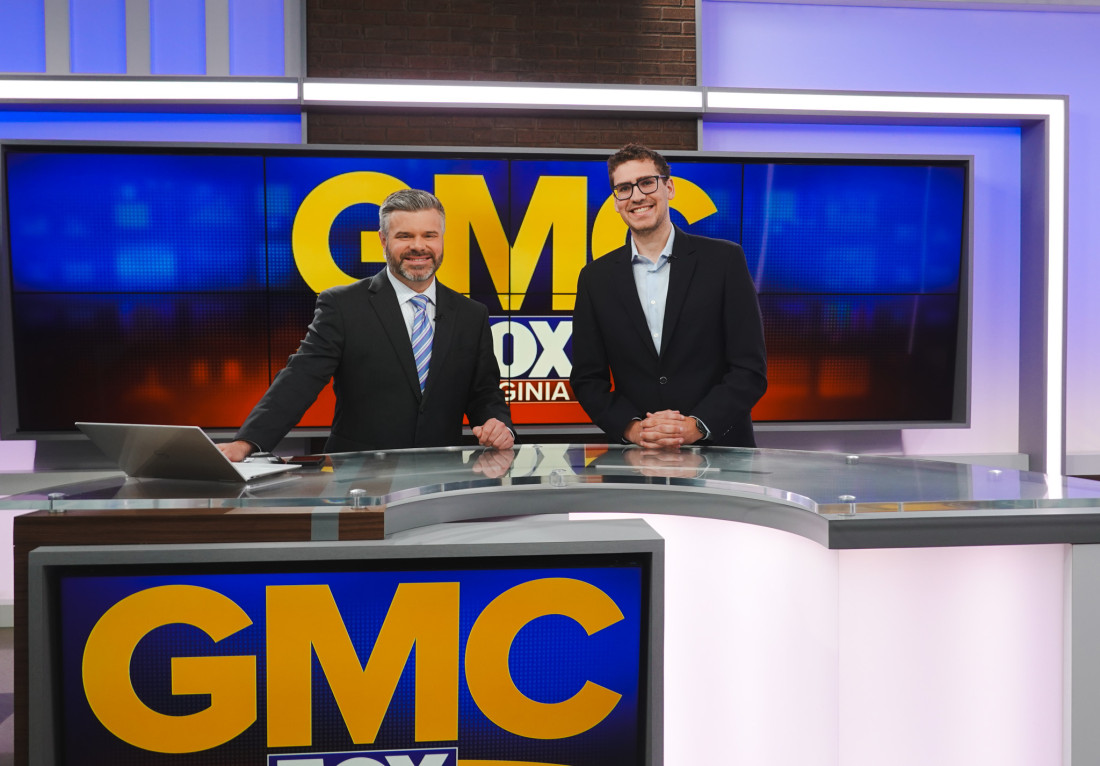 Jonathan stands with one news anchor, posing in front of the GMC logo.