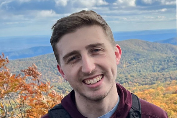 Alex Bass outdoors with fall season mountain vista behind him