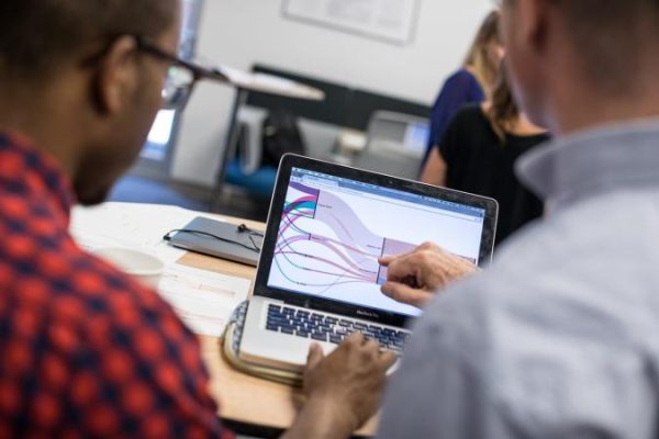 Two people discuss data visualization on a laptop screen displaying a flowchart.