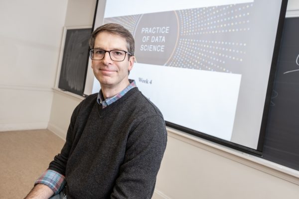 Brian Wright with glasses sits in a classroom in front of a projection screen displaying "Practice of Data Science, Week 4." 