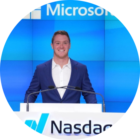 UVA Data Science MSDS Online Student Addison Nitto at NASDAQ podium with Microsoft logo on blue wall behind hime