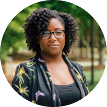 Dahlia Hylton wearing a black floral jacket and glasses in an outdoor environment