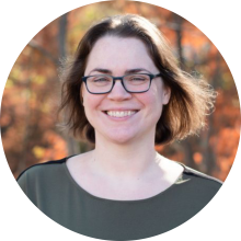 Jess wearing glasses and a grey shirt with a blurred autumn background.